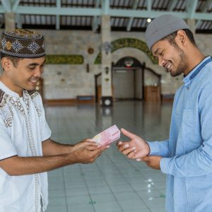 portrait of male muslim paying some zakat charity using cash at the mosque. indonesian money rupiah bank note for zakat